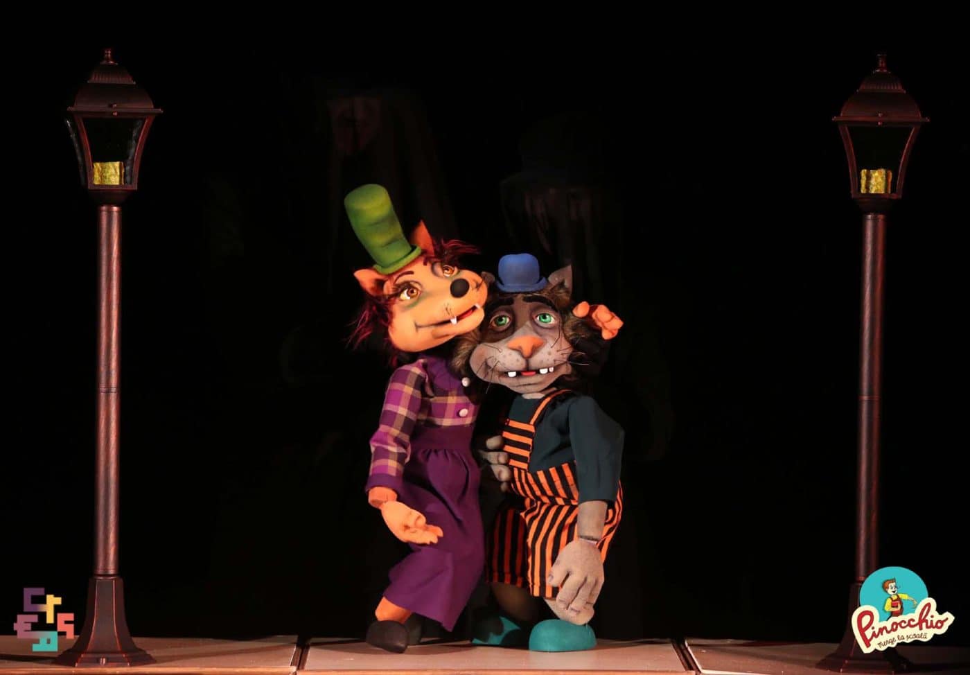 Personaje de teatru de păpuși cu costume colorate și pălării elegante, pe scenă.